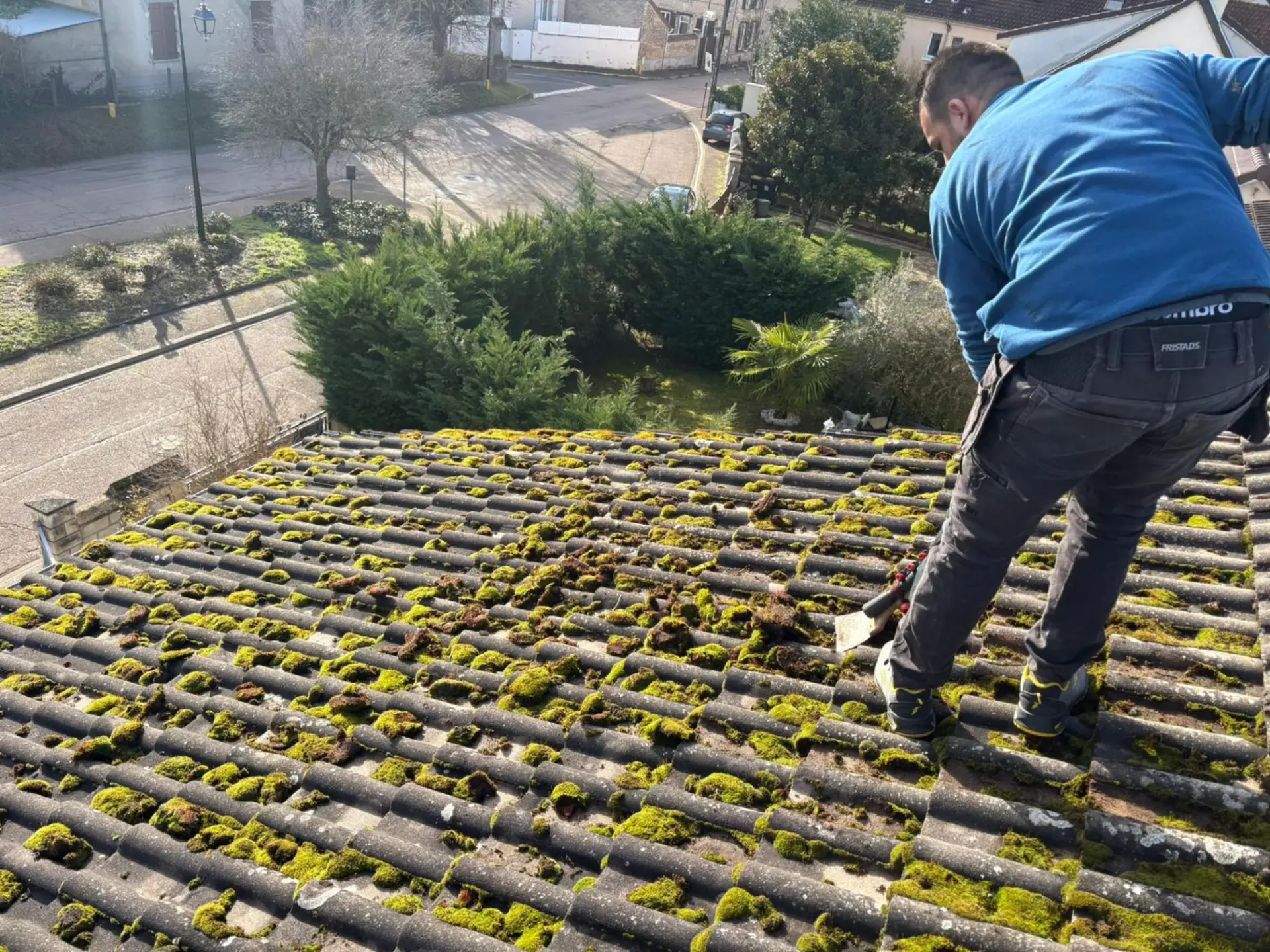 Couvreur de l'Entreprise Duval en plein démoussage manuel d'une toiture en tuiles à Giverny